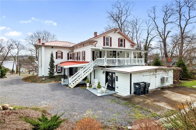 back of house with a chimney, stairs, covered porch, ac unit, and metal roof