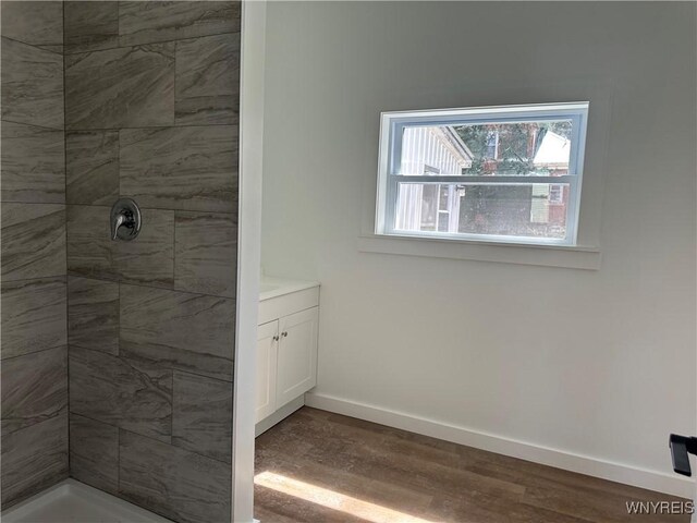 full bathroom featuring baseboards, wood finished floors, vanity, and a tile shower