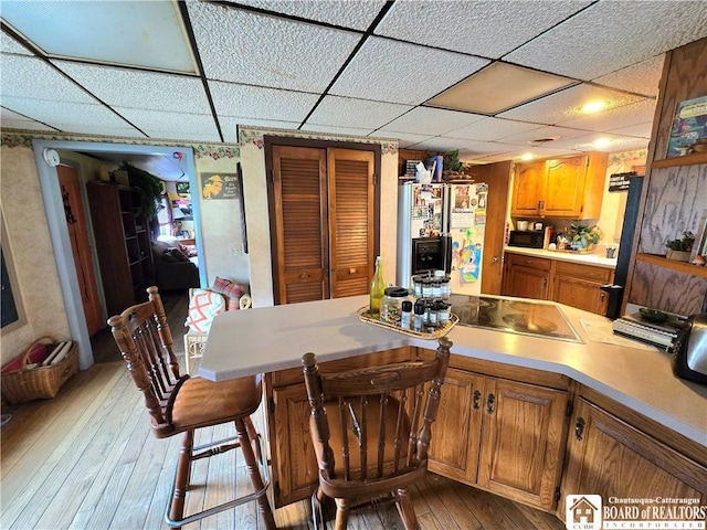 kitchen featuring brown cabinetry, black appliances, light wood-style floors, light countertops, and a paneled ceiling
