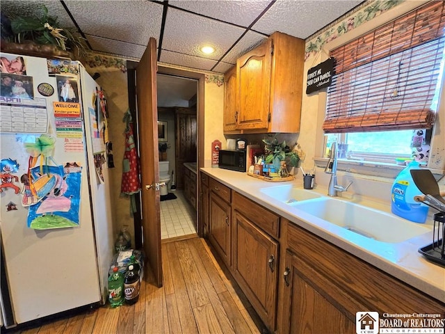 kitchen featuring light wood finished floors, light countertops, a sink, freestanding refrigerator, and brown cabinetry