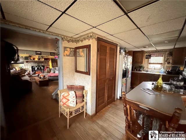 dining room featuring a warm lit fireplace, a drop ceiling, and light wood-type flooring