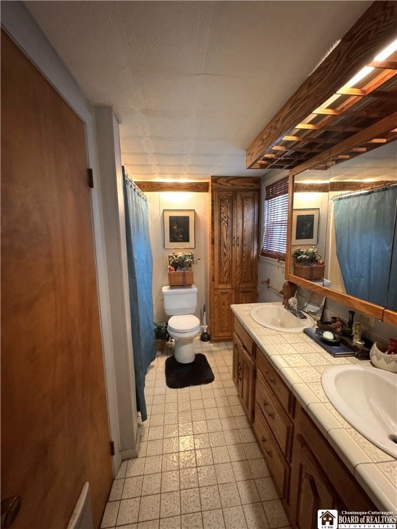 full bathroom with double vanity, tile patterned floors, toilet, and a sink