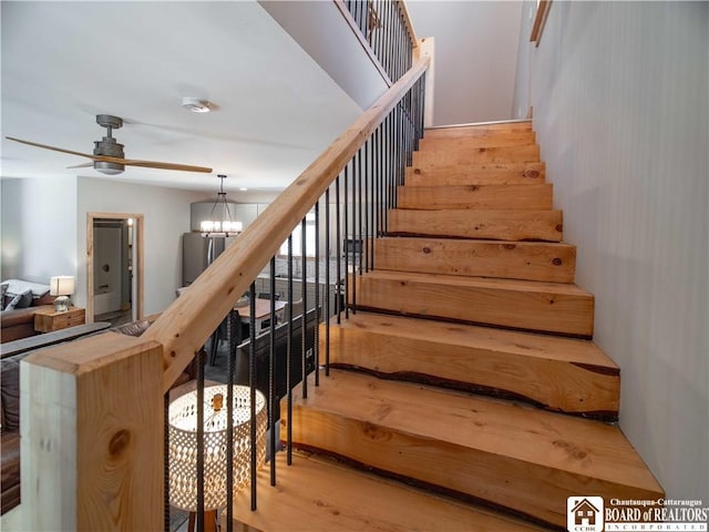 stairs with ceiling fan with notable chandelier and wood finished floors