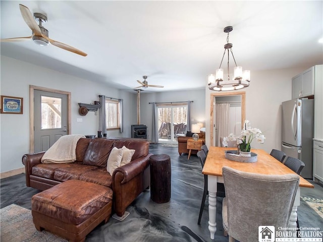 living area featuring ceiling fan with notable chandelier, finished concrete flooring, and a wood stove