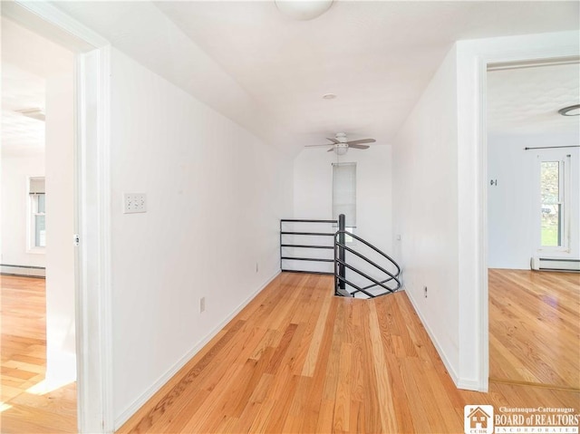 corridor with a baseboard radiator, baseboards, an upstairs landing, and light wood-type flooring