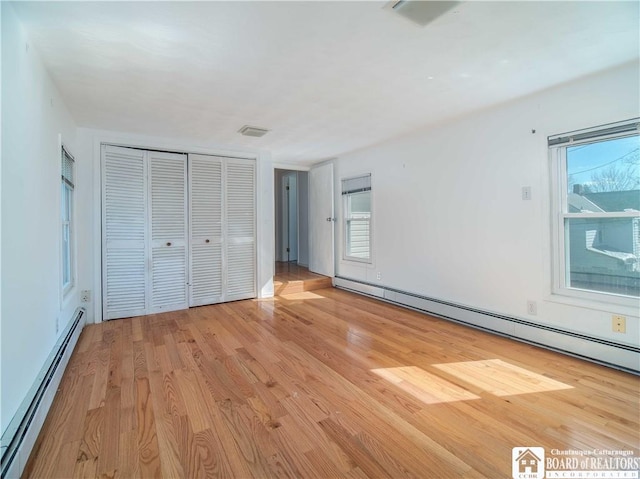 unfurnished bedroom with a baseboard heating unit, light wood-style floors, baseboard heating, and multiple windows
