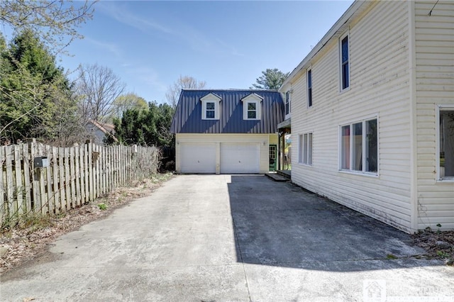view of property exterior featuring a detached garage, an outdoor structure, fence, metal roof, and a standing seam roof
