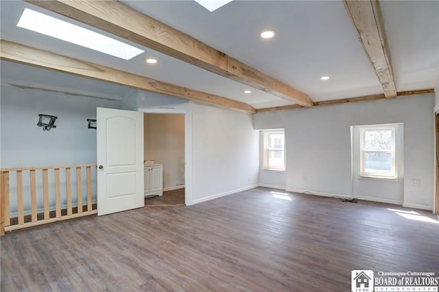 empty room featuring baseboards, wood finished floors, beamed ceiling, and a skylight
