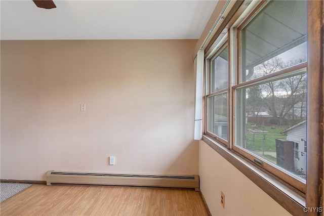 empty room featuring a healthy amount of sunlight, a baseboard heating unit, and wood finished floors