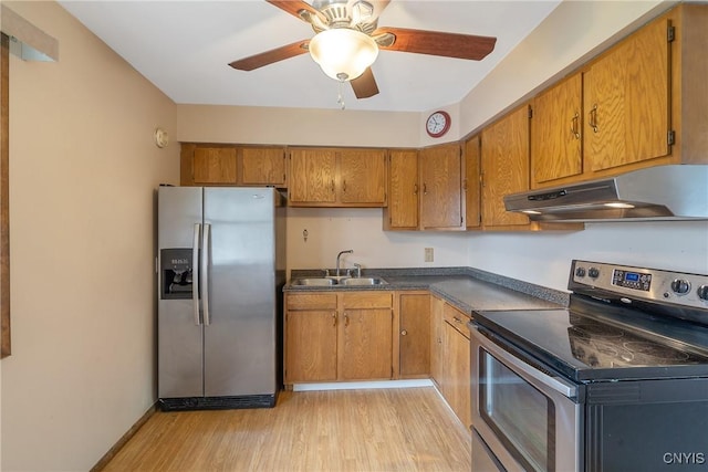 kitchen with appliances with stainless steel finishes, dark countertops, a sink, light wood-style floors, and under cabinet range hood