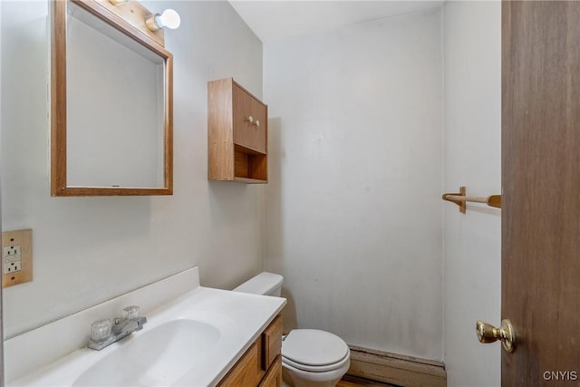 half bathroom with vanity, a baseboard heating unit, and toilet