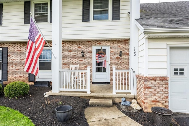 property entrance with brick siding, a garage, a shingled roof, and covered porch
