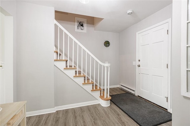 entryway featuring baseboard heating, baseboards, wood finished floors, and stairway