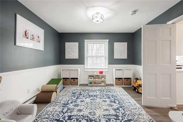 game room with wainscoting, a baseboard radiator, and wood finished floors