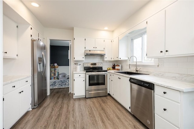 kitchen featuring stainless steel appliances, a sink, backsplash, light wood-style floors, and under cabinet range hood