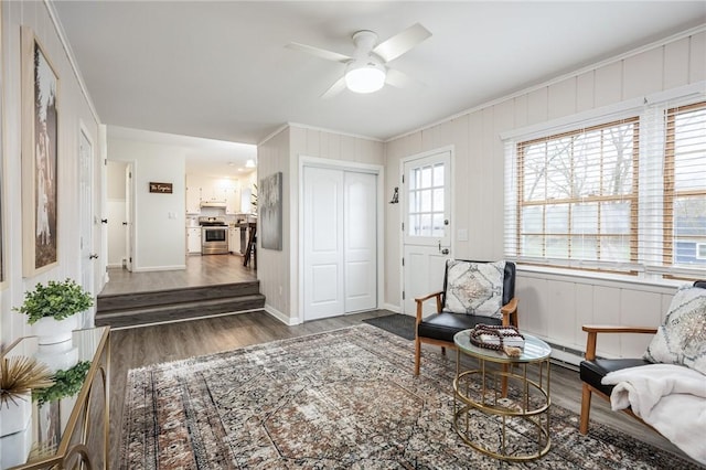 living area with wood finished floors, crown molding, baseboards, a baseboard radiator, and ceiling fan