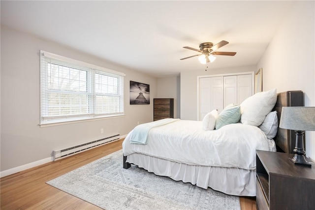 bedroom featuring a baseboard heating unit, baseboards, wood finished floors, and a closet