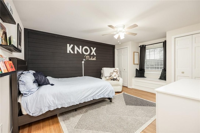 bedroom with light wood-style floors, multiple closets, a ceiling fan, and baseboards