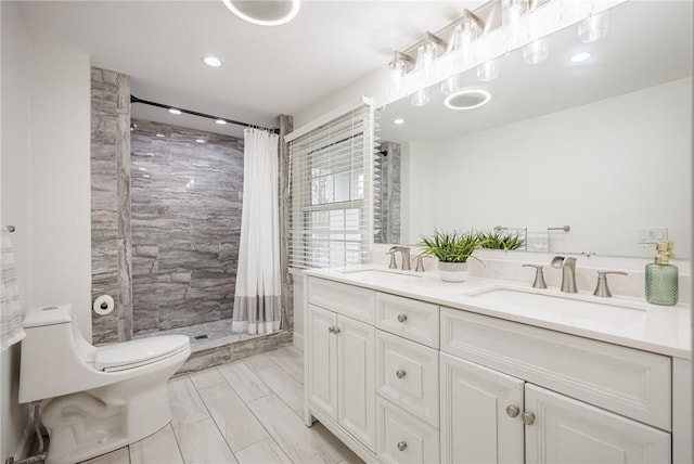 full bathroom with a tile shower, toilet, a sink, and double vanity
