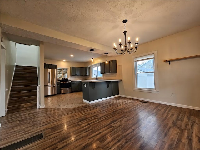 kitchen featuring a sink, a breakfast bar, an inviting chandelier, appliances with stainless steel finishes, and dark wood-type flooring