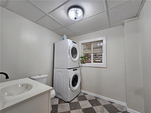 clothes washing area with baseboards, laundry area, stacked washer / dryer, and a sink
