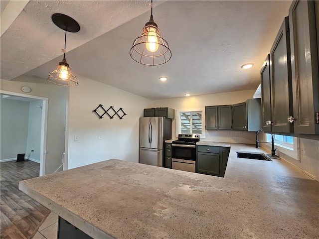 kitchen featuring stainless steel appliances, a sink, decorative light fixtures, baseboards, and a peninsula