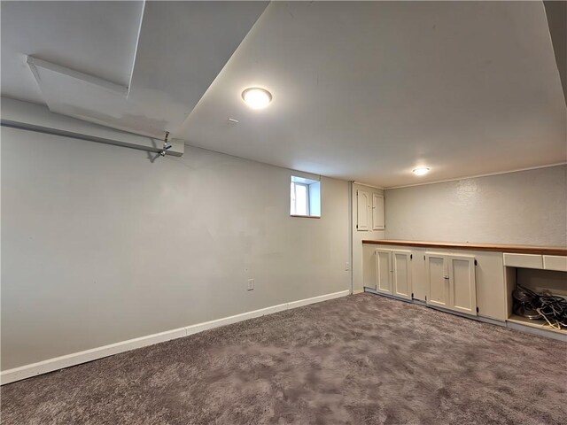 below grade area featuring baseboards and dark carpet