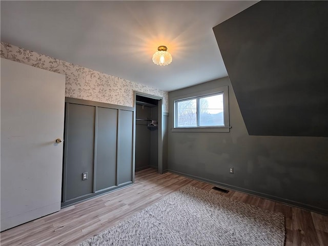 unfurnished bedroom featuring wallpapered walls, a closet, wainscoting, light wood-style floors, and visible vents