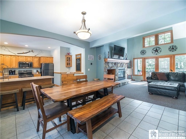 dining room featuring recessed lighting, a stone fireplace, light carpet, light tile patterned floors, and arched walkways
