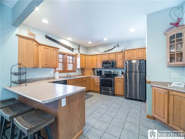 kitchen featuring a peninsula, a sink, a kitchen bar, light countertops, and appliances with stainless steel finishes