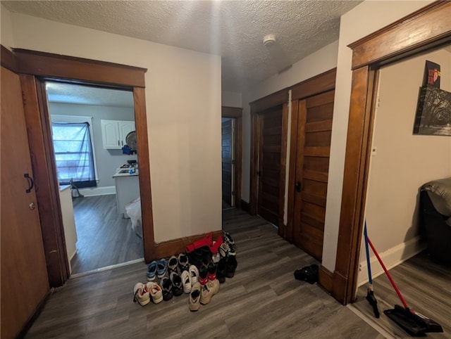 corridor featuring dark wood-type flooring, a textured ceiling, and baseboards