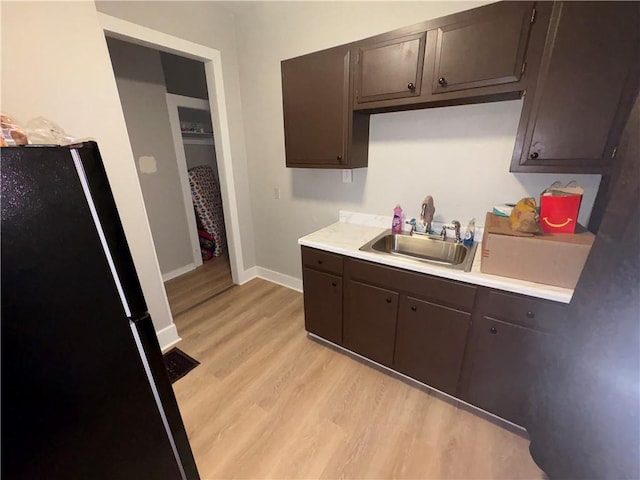 kitchen featuring light wood finished floors, a sink, dark brown cabinets, freestanding refrigerator, and light countertops