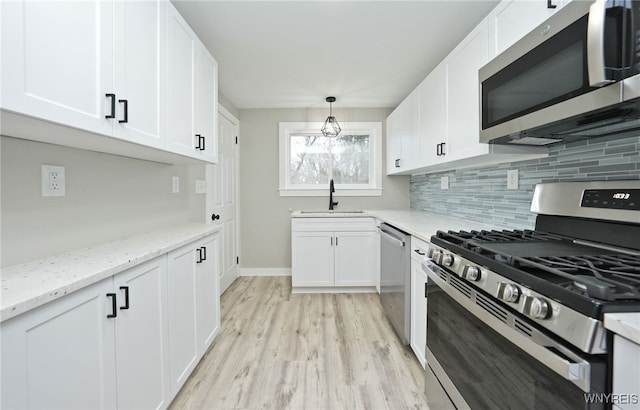 kitchen featuring a sink, light wood-style floors, white cabinetry, decorative backsplash, and appliances with stainless steel finishes