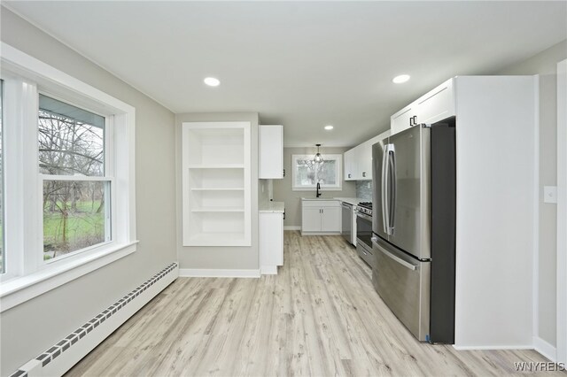 kitchen with appliances with stainless steel finishes, baseboard heating, white cabinetry, and a sink