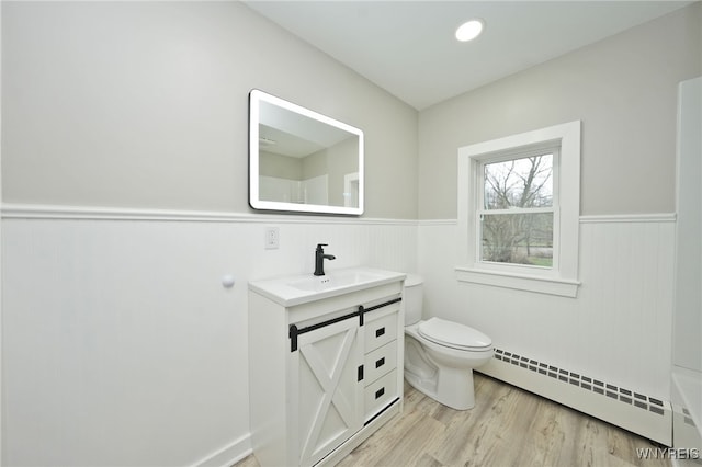 bathroom featuring a wainscoted wall, toilet, baseboard heating, wood finished floors, and vanity