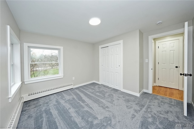 unfurnished bedroom with a baseboard radiator, baseboards, carpet flooring, and a closet