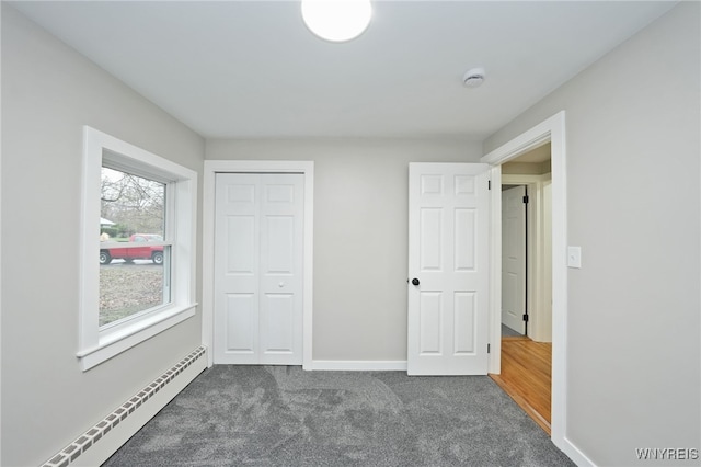 unfurnished bedroom with a baseboard heating unit, baseboards, dark carpet, and a closet