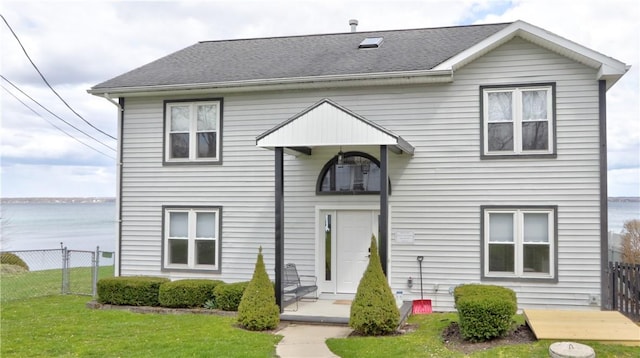 view of front of property featuring fence, a shingled roof, a front lawn, and a water view