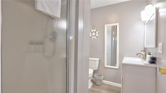 bathroom with a shower stall, wood finished floors, toilet, vanity, and baseboards