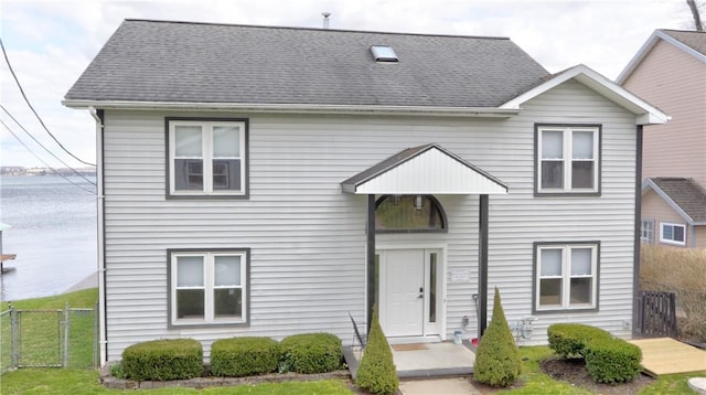 view of front of home featuring fence, a shingled roof, a front yard, and a water view