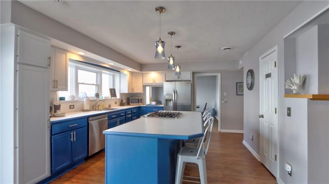 kitchen with a sink, a breakfast bar, light countertops, blue cabinetry, and appliances with stainless steel finishes