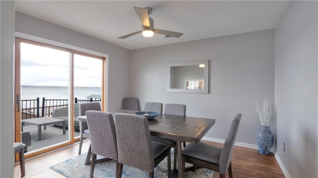 dining space with wood finished floors, a water view, baseboards, and ceiling fan