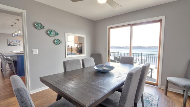 dining area with ceiling fan, baseboards, a water view, and light wood-style flooring