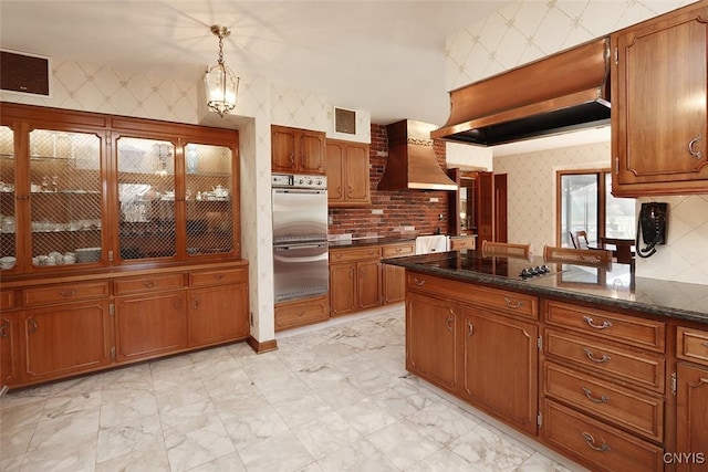 kitchen featuring wall chimney range hood, wallpapered walls, brown cabinets, black electric cooktop, and visible vents