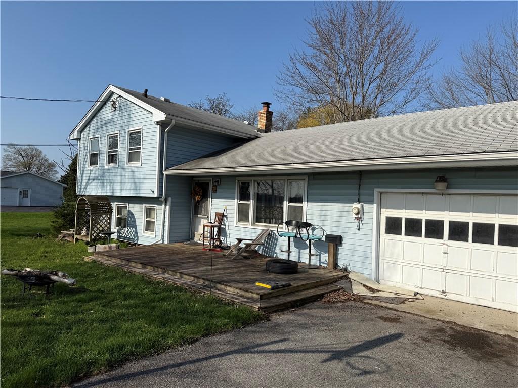 split level home with an attached garage, a chimney, a front yard, and a deck