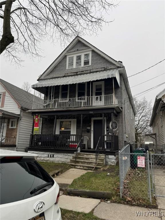 view of front of home featuring fence, covered porch, a balcony, and a gate