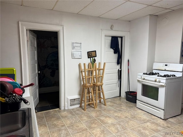 kitchen with a paneled ceiling, visible vents, and white gas range oven