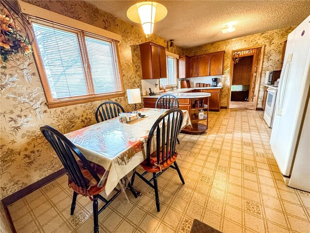dining room featuring wallpapered walls, a textured ceiling, and light floors