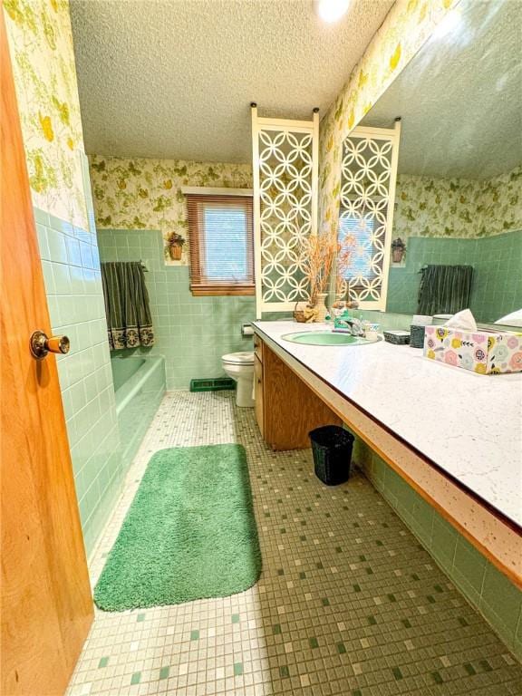 bathroom with a textured ceiling, toilet, a bathing tub, wallpapered walls, and vanity