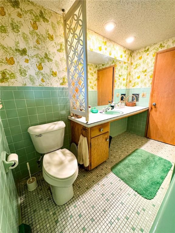 bathroom featuring a wainscoted wall, wallpapered walls, and tile walls